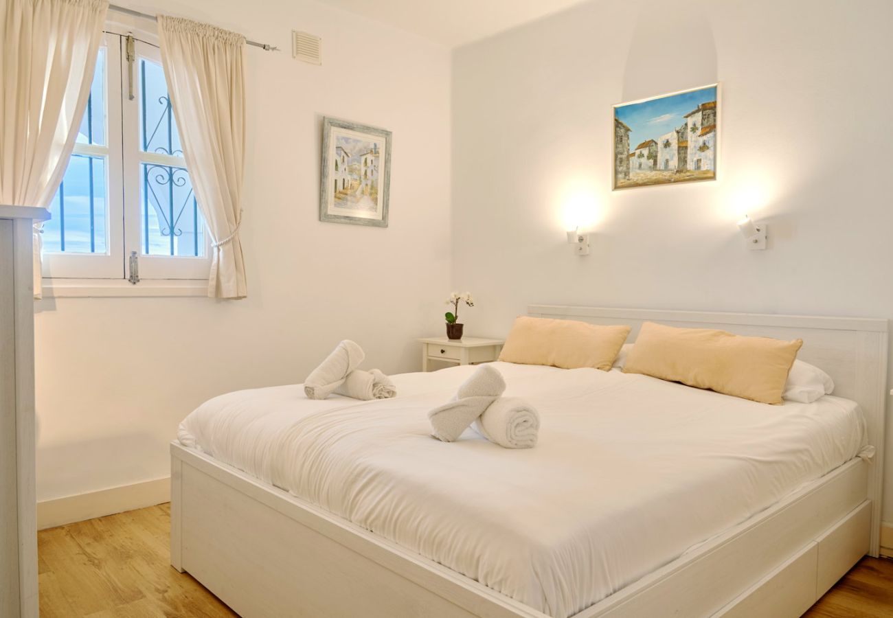 Master bedroom med dubbelsäng och naturligt ljus i semesterlägenhet.